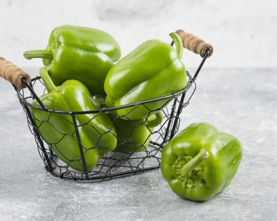 Green bell peppers in a metallic basket on marble background. High quality photo